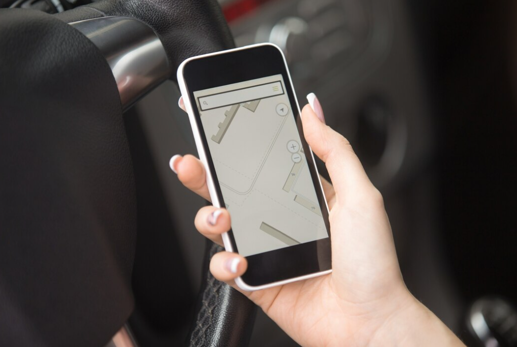 a hand holding smartphone with a map on it inside the car